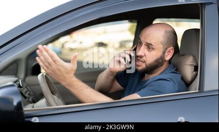 Mann, der im Auto sitzt und während der Fahrt mit dem Mobiltelefon telefoniert. Abgelenkt schockierter Kerl nicht aufmerksam auf der Straße mit Smartphone genervt durch schlechte Nachrichten Stockfoto