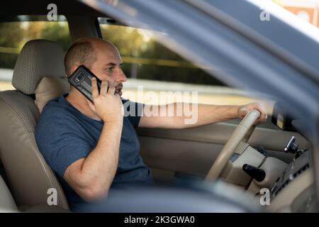 Mann mittleren Alters mit Telefon während der Fahrt mit dem Auto. Transport und Fahrzeug Stockfoto