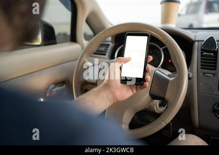 Nahaufnahme der männlichen Hand mit Smartphone mit weißem Modell auf dem Bildschirm, Hintergrund des Autolenkrads, Positionssuche über gps-Navigator Stockfoto