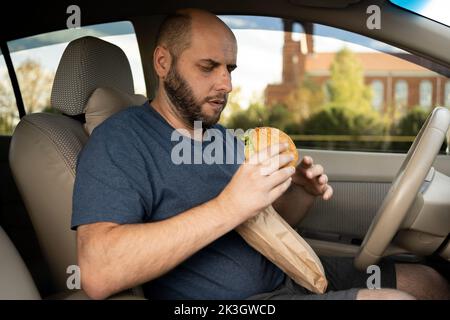 Taxifahrer essen Burger im Auto, da der Verkehr am Morgen sehr schlecht ist. Essen Sie Hamburger im Auto Stockfoto