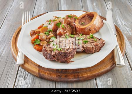 Ossobuco mit Gemüse auf Teller mit Messer und Gabel auf Holzhintergrund Stockfoto