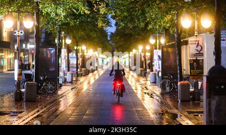 Hannover, Deutschland. 27. September 2022. Ein Radfahrer fährt am frühen Morgen zwischen den Straßenlaternen im Stadtzentrum. Die von den Bundesregierungen aufgrund der Energiekrise eingeführten Energiesparregelungen führen nicht zu dunklen Downtowns. Beleuchtete Werbetafeln müssen am folgenden Tag von 10:4 Uhr bis 22:00 Uhr ausgeschaltet werden. Schaufenster und Straßenbeleuchtung sind jedoch von den Verordnungen ausgenommen. Quelle: Julian Stratenschulte/dpa/Alamy Live News Stockfoto