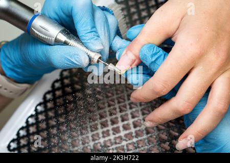 Verarbeiten Sie professionelle Hardware Maniküre. Manikuristin in blauen Handschuhen arbeitet mit Fräser und entfernt alte Gelpolitur von Frau Client Nägel. Elektr Stockfoto