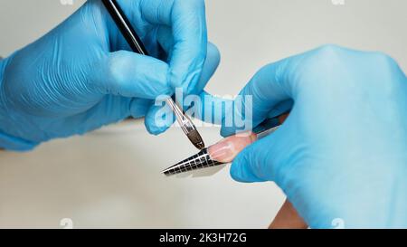 Konstruktion von Schönheitsnägeln. Untere Nagelverlängerung. Master Manikurist im Schönheitssalon erhöht Nägel durch Verlängerung Client Nagelplatte mit Acryl oder g Stockfoto