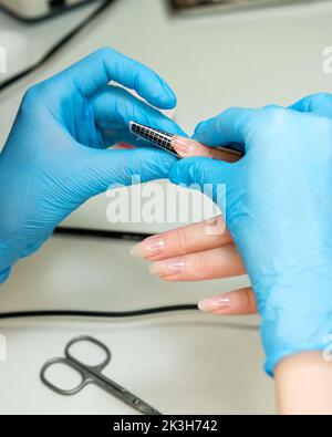 Konstruktion von Schönheitsnägeln. Untere Nagelverlängerung. Master Manikurist im Schönheitssalon setzt spezielle Papierformen unter Nagel erhöhen Länge weibliche Client Stockfoto