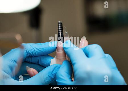 Konstruktion von Schönheitsnägeln. Untere Nagelverlängerung. Meister Manikurist im Schönheitssalon prüft, ob Papier Formen für Nagelverlängerung gleichmäßig fem installiert Stockfoto