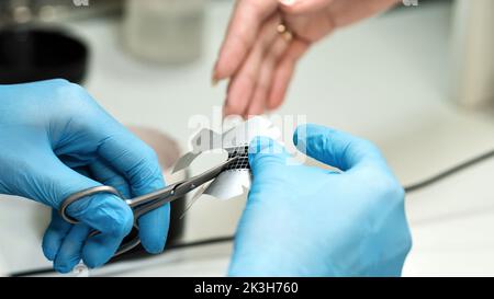 Konstruktion von Schönheitsnägeln. Untere Nagelverlängerung. Master Manikurist im Schönheitssalon hält eine Papierform für Nagelverlängerung. Maniküre. Fingernägel Stockfoto