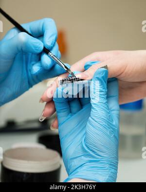 Konstruktion von Schönheitsnägeln. Untere Nagelverlängerung. Master Manikurist im Schönheitssalon erhöht Nägel durch Verlängerung Client Nagelplatte mit Acryl oder g Stockfoto