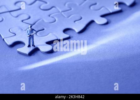 Konzept des ruhigen Aufenschens, Job Burnout, Depression. Blauer monochromer Hintergrund. Einzelne kleine Arbeiter Miniatur-Figur am Rand des verbundenen Puzzle Stockfoto