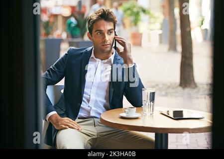 Immer für seine Kunden verfügbar. Ein junger Geschäftsmann, der sich mit seinem Handy unterhielt, während er in einem Café im Freien Kaffee getrunken hatte. Stockfoto