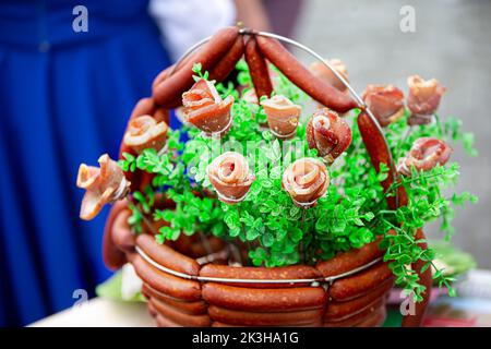 Ein festlicher Korb mit Fleischprodukten, wunderschön mit viel Grün dekoriert. Stockfoto