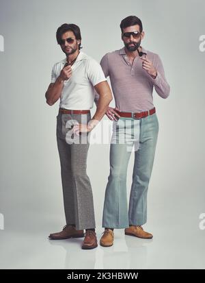 Wir wissen, dass sie groovig waren. Studioaufnahme von zwei Männern, die zusammen stehen, während sie Retro 70s tragen und Pfeifen rauchen. Stockfoto