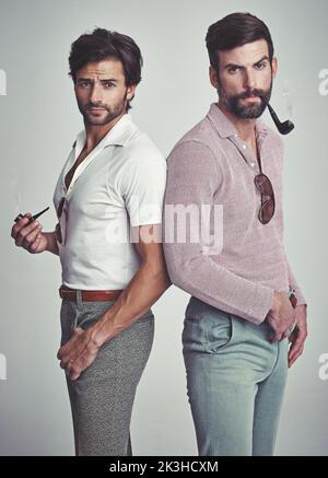 Wir wissen, dass sie groovig waren. Studioaufnahme von zwei Männern, die zusammen stehen, während sie Retro 70s tragen und Pfeifen rauchen. Stockfoto