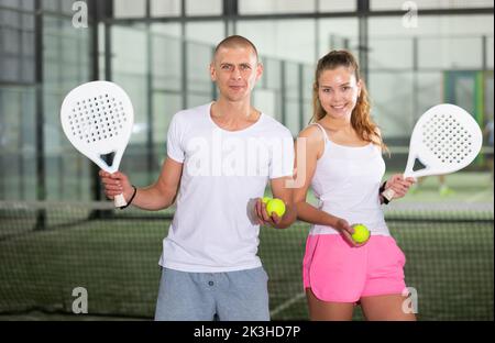 Paar mit Padel-Schlägern, die auf dem Tennisplatz posieren Stockfoto