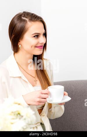 Weibliche kaukasische Klientin mit einer Tasse Kaffee in den Händen lächelnd über den Termin eines Arztes Stockfoto