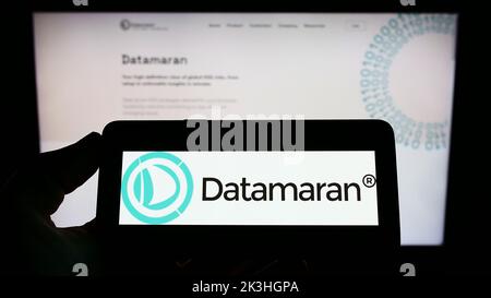 Person, die Mobiltelefon mit Logo des britischen Software-Unternehmens Datamaran Ltd. Auf dem Bildschirm vor der Business-Webseite hält. Konzentrieren Sie sich auf die Telefonanzeige. Stockfoto