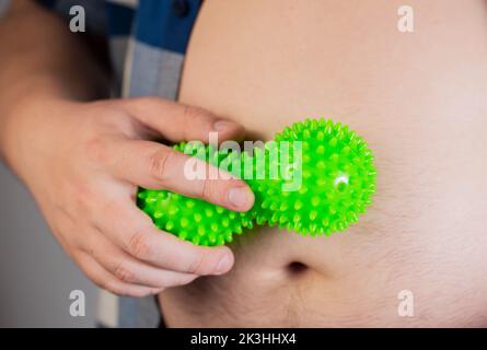 Ein Mann in einem Hemd rollt ein Bauchmassager, um Fett zu verbrennen. Anti-Cellulite-Verfahren. Abnehmen. Übergewicht Stockfoto