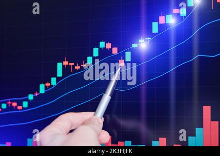 Der Trader zeigt mit einem Stift auf den Rising Stock Chart auf dem Monitor Stockfoto