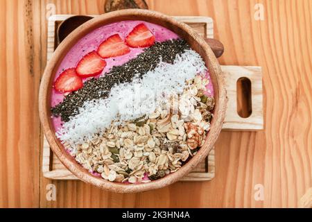 Köstliches gesundes Frühstück, Erdbeer-Smoothie-Schale mit Müsli, Früchten, Chiasamen und Kokosnuss, eine ästhetische Aufnahme auf hellem Hintergrund. Stockfoto