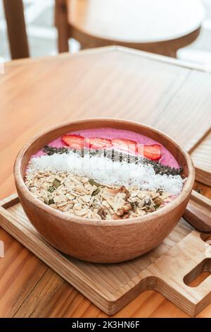 Köstliches gesundes Frühstück, Erdbeer-Smoothie-Schale mit Müsli, Früchten, Chiasamen und Kokosnuss, eine ästhetische Aufnahme auf hellem Hintergrund. Stockfoto