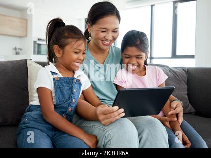 Glückliche Mutter und Kinder mit digitalem Tablet sehen lustige Videos, Filme oder Spiele auf dem heimischen Sofa. Familie genießen Sie Comedy-Cartoon mit Tech Stockfoto