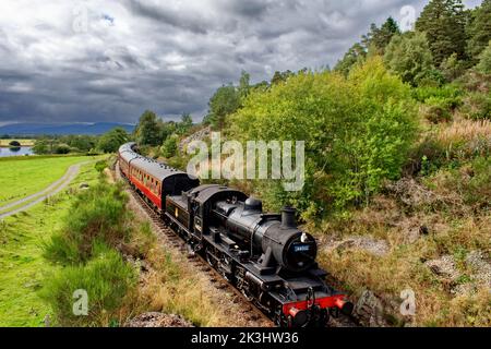 STRATHSPEY DAMPFEISENBAHN SCHOTTLAND EIN ZUG NÄHERT SICH BROOMHILL STATION FLUSS SPEY UND CAIRNGORMS IM HINTERGRUND Stockfoto