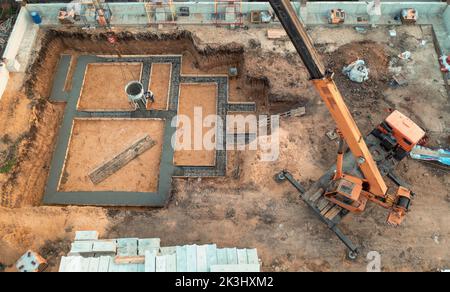 Gründung eines zukünftigen Hauses. Gießfundament mit Zement auf Baustelle mit Kran, Luftaufnahme. Stockfoto