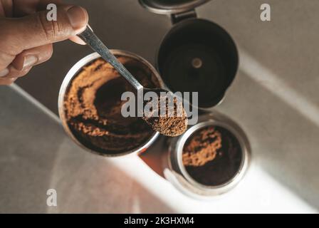 Kaffeemaschine aus Metall zum Brühen von Espresso auf dem Herd. Teelöffel mit gemahlenen Kaffeebohnen. Hochwertige Fotos Stockfoto