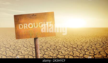 Ein rostiger Schild mit der Aufschrift DÜRRE auf dem Hintergrund einer Wüste mit rissigem Boden Stockfoto