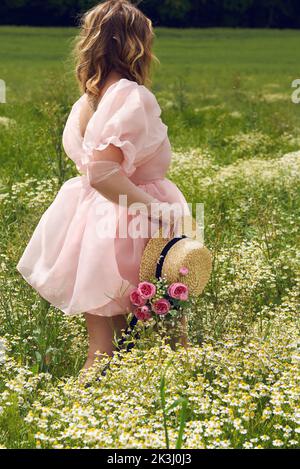 Im Sommer trägt eine junge blonde Frau in einem rosa geschwollenen Kleid auf einem Blumenfeld Stockfoto