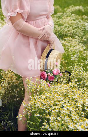 Im Sommer trägt eine junge blonde Frau in einem rosa geschwollenen Kleid auf einem Blumenfeld Stockfoto