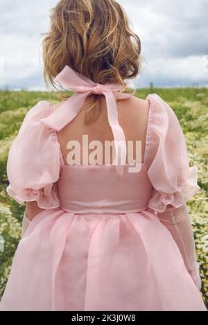 Im Sommer trägt eine junge blonde Frau in einem rosa geschwollenen Kleid auf einem Blumenfeld Stockfoto