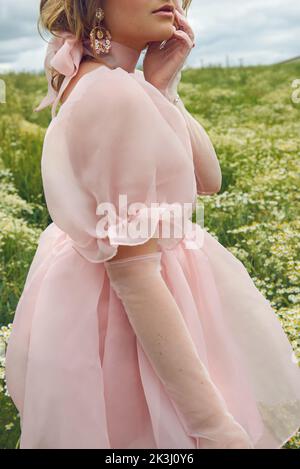 Im Sommer trägt eine junge blonde Frau in einem rosa geschwollenen Kleid auf einem Blumenfeld Stockfoto