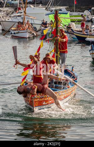 Das jährliche Fest der 'U Pisci a Mari' im sizilianischen Dorf Aci Trezza, in der Nähe von Catania. Dies findet um das Fest der Geburt des hl. Johannes des Täufers Ende Juni statt. Es handelt sich um eine traditionelle Fischereiexpedition für Schwertfisch, die früher in der Straße von Messina stattgefunden hat. Die Rolle des Schwertfisches wird von einem Schwimmer gespielt, der wiederholt von den Fischern gefangen wird, blutig aufgeschnitten wird, dann aber irgendwie entkommen kann. Schließlich schafft es der „Schwertfisch“, das Boot umzustürzen. (Den „Schwertfisch“ aufschneiden) Stockfoto