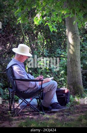 Ein einsitzender älterer Mann, der in schattiger Lichtung saß und schrieb Stockfoto