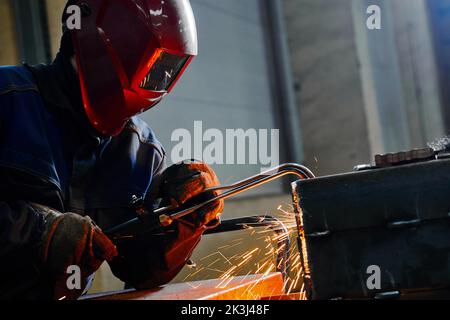 Mitarbeiter mit Maske schneidet Balken mit Heißgasabschneider im Werk Stockfoto