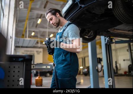 Erfahrener Autotechniker, der ein Arbeitswerkzeug inspiziert Stockfoto