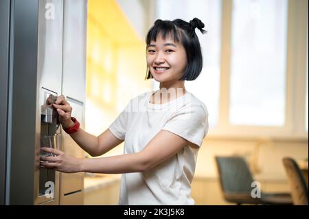 Fröhliche Frau, die ein Glas mit Wasser aus dem Kühlschrank füllte Stockfoto