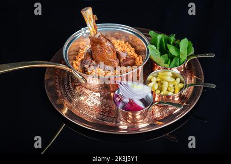 Traditionelle türkische Küche Lammschenkel und Reis. Langsam gekochter Lammschenkel. Lammschenkel serviert auf einem Kupfertablett und in einer Kupferschale. Stockfoto