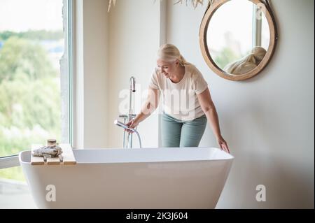 Erwachsene Frau, die das Bad mit Wasser füllte Stockfoto