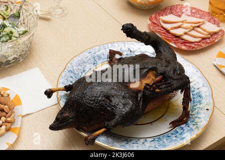 Verbrannter Vogelkadaver auf dem Servierteller auf dem Esstisch. Servieren Sie verkohlte Gerichte. Miserable Hausfrau und schlechter Koch. Leckere kalte Vorspeisen und schrecklich Stockfoto