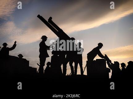 Soldaten, die gegen den Himmel silhouettiert wurden, bereiten sich darauf vor, eine Luftabwehrkanone abzufeuern. Rechts auf dem Foto wird einem Soldaten eine große Schale für die Waffe übergeben. Die Schlacht von Broodseinde war Teil der dritten Schlacht von Ypern von 1917 – die von Sir Douglas Haig entwickelt wurde, um den Passchendaele-Grat zu erobern. Stockfoto