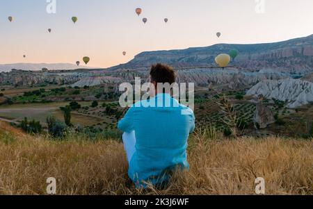 Junge Männer beobachten Heißluftballons während des Sonnenaufgangs in Kappadokien Türkei, Kapadokya Goreme. Junge kaukasische Männer beobachten den Sonnenaufgang im Tal der Kappadokien-Türkei Stockfoto