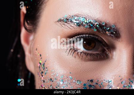 Nahaufnahme der jungen Frau mit funkelnd Glitter auf Augenbraue und Gesicht isoliert auf schwarz, Stock Bild Stockfoto
