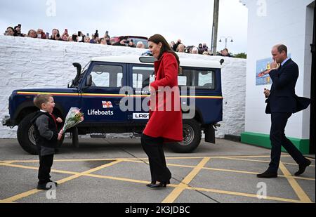 Der Prinz von Wales (rechts) sieht zu, wie seine Frau, die Prinzessin von Wales, von dem vierjährigen Theo Crompton bei ihrem Besuch der RNLI Holyhead Lifeboat Station in Anglesey, Nordwales, mit einer schicken Blumenpracht überreicht wird, wo sie sich mit der Crew traf, Freiwillige und einige von denen, die von ihrer lokalen Einheit unterstützt wurden. Bilddatum: Dienstag, 27. September 2022. Stockfoto