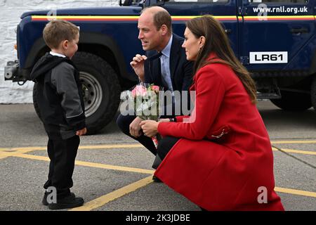 Der Prinz von Wales (Mitte) zeigt, wie seine Frau, die Prinzessin von Wales, von dem vierjährigen Theo Crompton bei ihrem Besuch in der RNLI Holyhead Lifeboat Station in Anglesey, Nordwales, eine schicke Blumenpracht erhalten wird, wo sie sich mit der Crew treffen, Freiwillige und einige von denen, die von ihrer lokalen Einheit unterstützt wurden. Bilddatum: Dienstag, 27. September 2022. Stockfoto