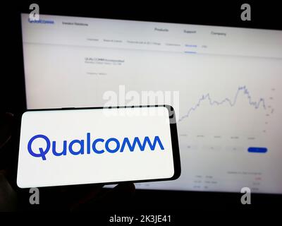 Person, die das Smartphone mit dem Logo des US-Halbleiterunternehmens Qualcomm Incorporated auf dem Bildschirm vor der Website hält. Konzentrieren Sie sich auf die Telefonanzeige. Stockfoto