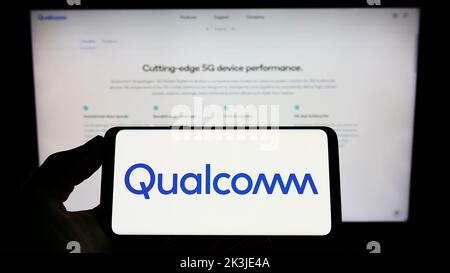 Person mit Mobiltelefon und Logo des US-Halbleiterunternehmens Qualcomm Incorporated auf dem Bildschirm vor der Webseite. Konzentrieren Sie sich auf die Telefonanzeige. Stockfoto