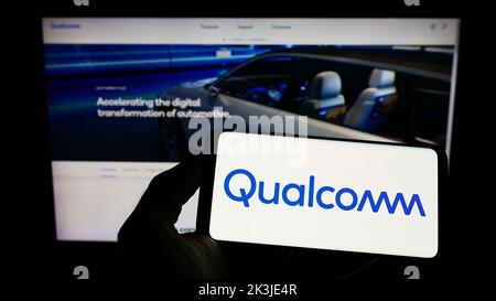 Person mit Mobiltelefon und Logo des amerikanischen Halbleiterunternehmens Qualcomm Incorporated auf dem Bildschirm vor der Webseite. Konzentrieren Sie sich auf die Telefonanzeige. Stockfoto