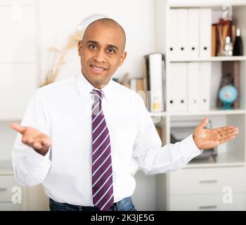 Wir begrüßen Büroangestellte in einem leichten Hemd und binden lächelnd und mit Gesten, damit wir eintreten können Stockfoto